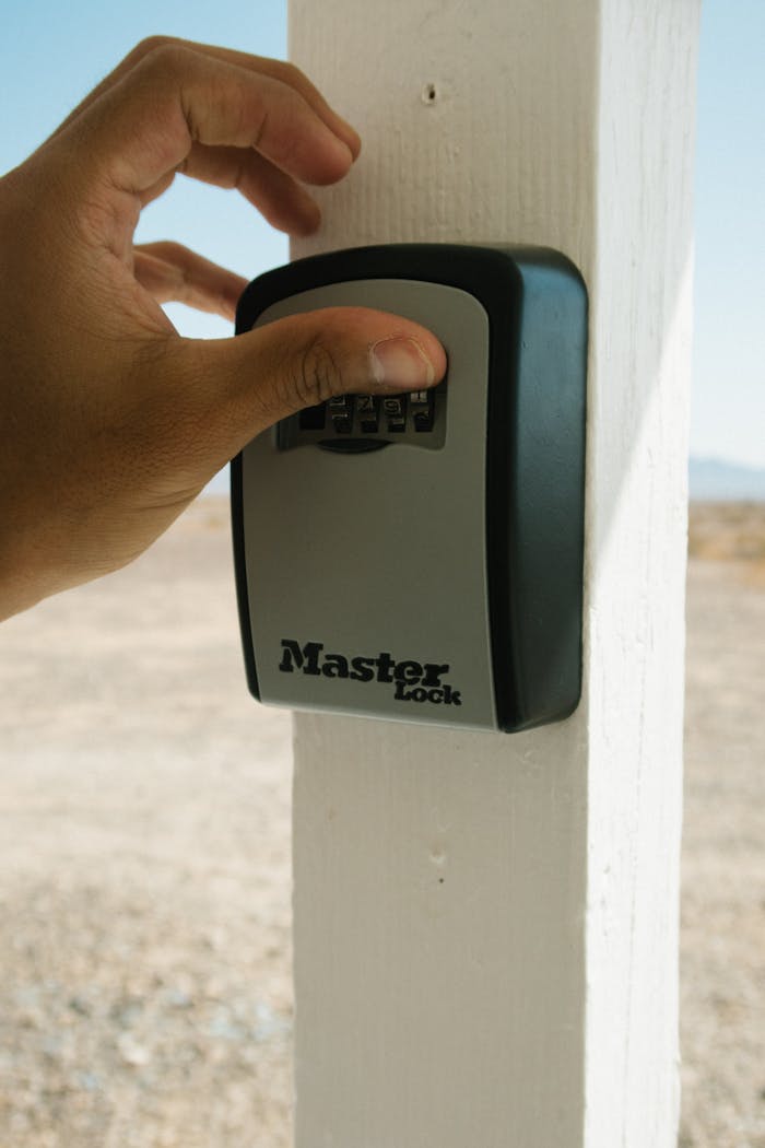 about-02 Hand operating a combination lockbox outdoors, emphasizing security and safety.